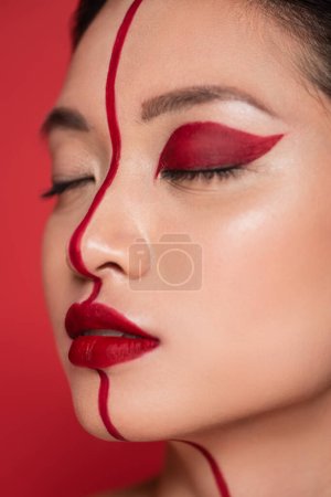 close up portrait of asian woman with closed eyes and creative visage on face divided with line isolated on red