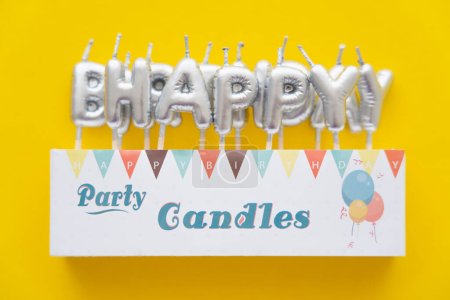 Vista superior de las velas en forma de letras de Feliz Cumpleaños sobre fondo amarillo 