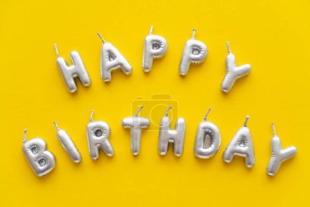 Draufsicht auf festliche Kerzen in Form von Happy Birthday Schriftzug auf gelbem Hintergrund 