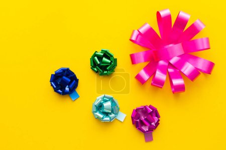 Top view of shiny gift bows on yellow background 