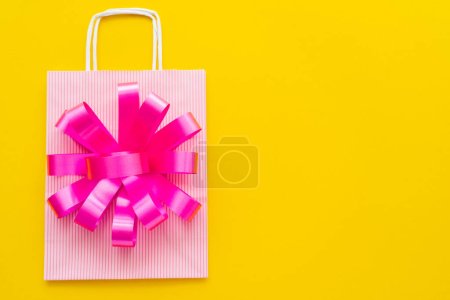 Top view of gift bow and shopping bag on yellow background 