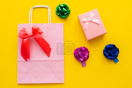Photo for Top view of shopping bag and gift bows near present on yellow background - Royalty Free Image