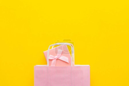 Draufsicht auf rosa Geschenkbox und Einkaufstasche auf gelbem Hintergrund 