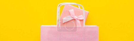 Top view of pink present and striped shopping bag on yellow background, banner 