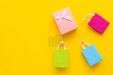 Top view of pink gift box and small shopping bags on yellow background 