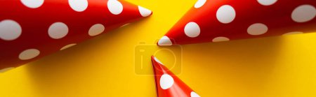 Top view of red dotted party caps on yellow background, banner 