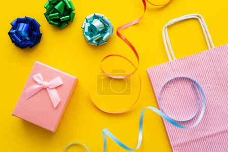 Top view of gift bows near present and shopping bag on yellow background 