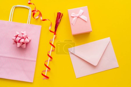 Top view of pink envelope near present and shopping bag on yellow background 