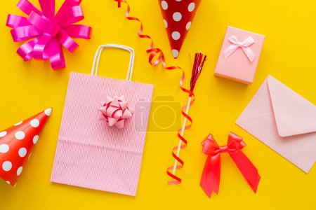 Photo for Top view of gift box near party caps and shopping bag on yellow background - Royalty Free Image