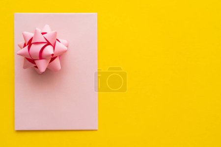 Top view of pink greeting card with gift bow on yellow background with copy space 