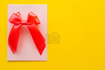 Top view of bow on greeting card on yellow background 