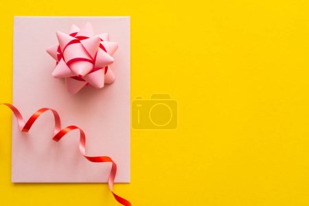 Top view of gift bow and serpentine on greeting card on yellow background 