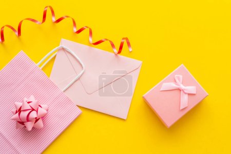 Top view of pink shopping bag near envelope and present on yellow background 