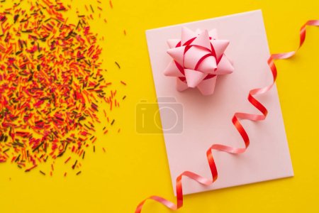 Photo for Top view of pink greeting card with gift bow and blurred sprinkles on yellow background - Royalty Free Image
