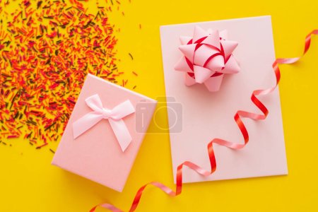 Top view of festive gift and greeting card near blurred sprinkles on yellow background 