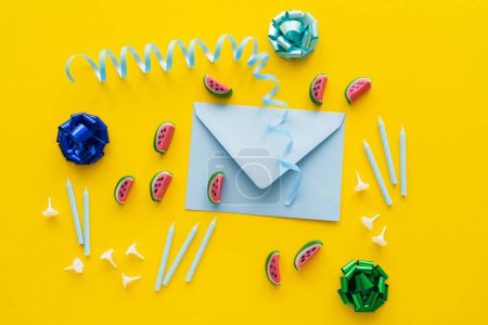Top view of festive candles near sweets and envelope on yellow background 