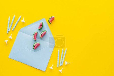 Top view of candies on envelope near festive candles on yellow background 