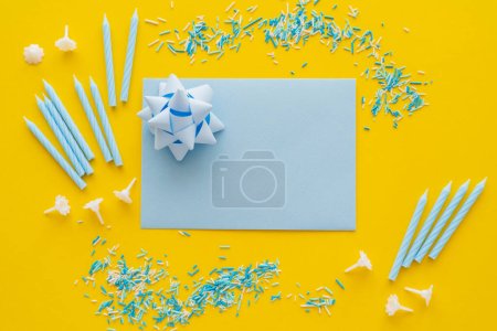Top view of greeting card with gift bow and blue candles on yellow background 