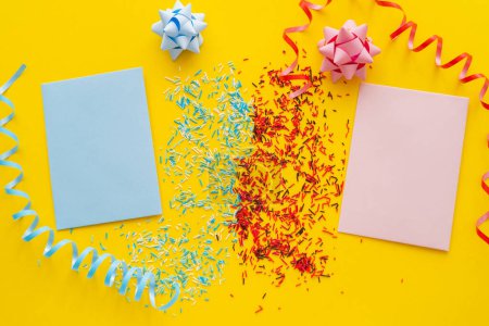 Top view of blue and pink greeting cards near sprinkles and serpentine on yellow background 