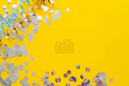Top view of colorful serpentine and confetti on yellow background 