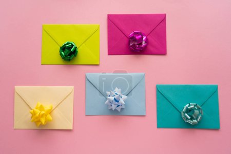 Vue du dessus des noeuds cadeaux colorés sur des enveloppes sur fond rose 