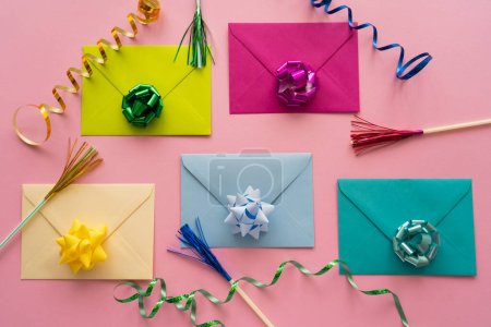 Top view of colorful gift bows on envelopes near serpentine on pink background 