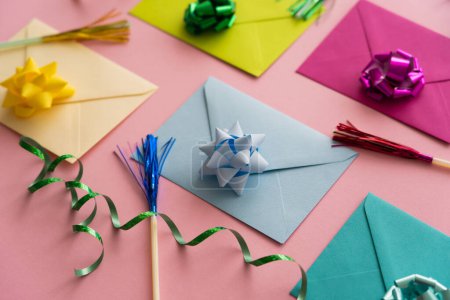 Close up view of colorful envelopes with gift bows near serpentine on pink background 
