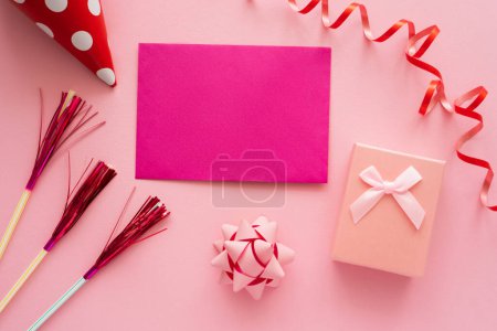 Draufsicht auf rosa Grußkarte in der Nähe von Geschenkbox und Serpentin auf rosa Hintergrund 
