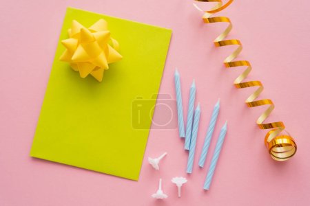 Top view of greeting card near serpentine and festive candles on pink background 