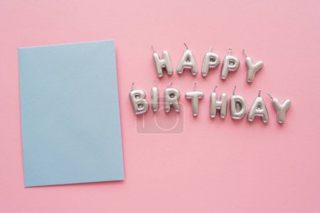 Top view of greeting card near candles in shape of Happy Birthday lettering on pink background 