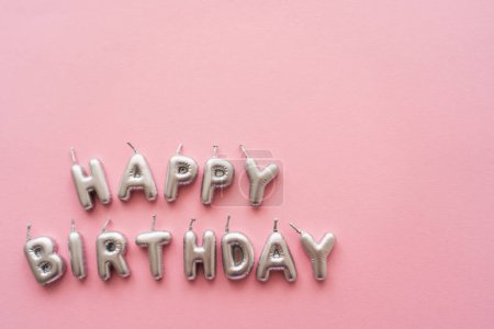 Top view of silver candles in shape of Happy Birthday lettering on pink background 