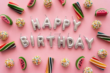 Widok z góry kolorowe cukierki w pobliżu świec w kształcie Happy Birthday napisy na różowym tle 