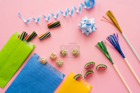 Top view of candies near paper bags and serpentine on pink background 