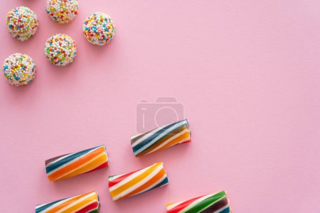 Flache Lage mit gestreiften und bunten Bonbons auf rosa Hintergrund 