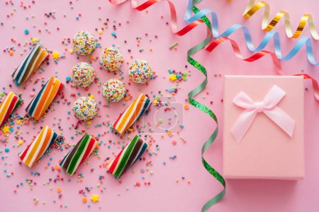 Top view of gift box near serpentine and colorful candies on pink background 
