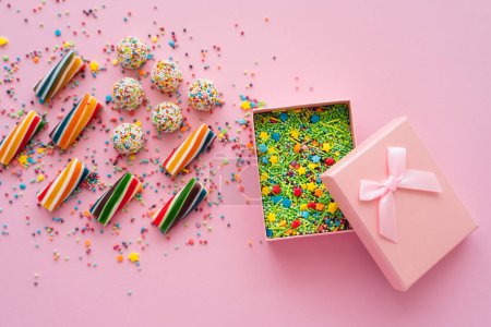 Top view of colorful sweets near gift box with sprinkles on pink background 