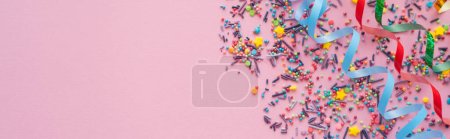 Top view of different colorful sprinkles and serpentine on pink background, banner 