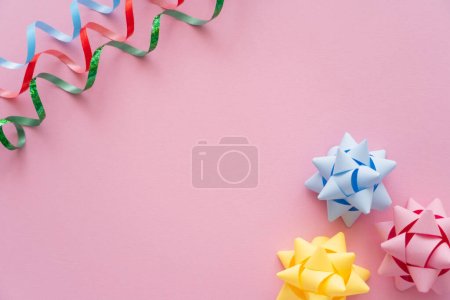 Top view of colorful serpentine and gift bows on pink background 
