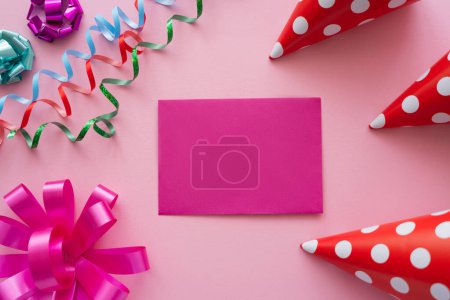Photo for Top view of empty greeting card near serpentine and party caps on pink background - Royalty Free Image