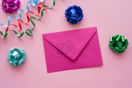 Draufsicht des Umschlags in der Nähe von Geschenkbögen und Serpentinen auf rosa Hintergrund 