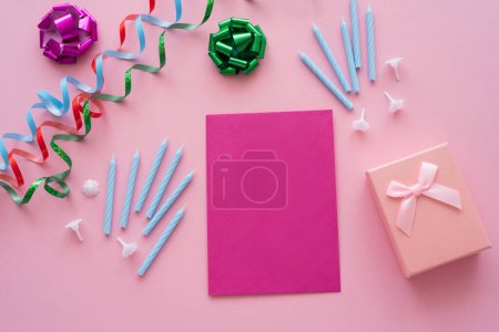Top view of empty greeting card near candles and present on pink background 