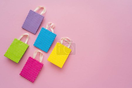 Foto de Vista superior de pequeñas bolsas de compras punteadas sobre fondo rosa con espacio para copiar - Imagen libre de derechos