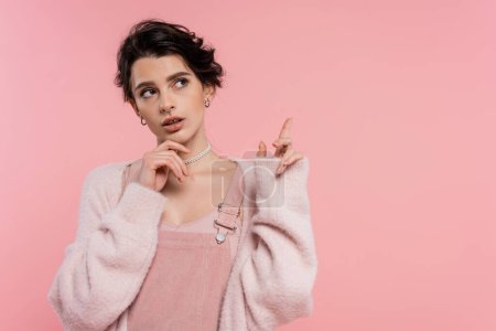Photo for Thoughtful brunette woman touching chin and pointing with finger isolated on pink - Royalty Free Image