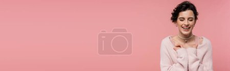 Téléchargez les photos : Joyeuse jeune femme en cardigan chaud riant les yeux fermés isolés sur rose, bannière - en image libre de droit