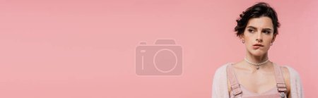 Téléchargez les photos : Offensé femme brune en collier de perles mordant lèvre et regardant loin isolé sur rose, bannière - en image libre de droit