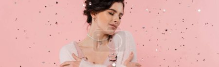 pretty brunette woman in cozy cardigan standing with closed eyes near confetti on pink background, banner