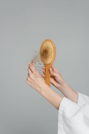 vue partielle de la jeune femme tenant une brosse à cheveux en bois et tirant les cheveux abîmés isolés sur gris 