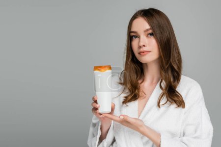 Téléchargez les photos : Jeune femme aux cheveux brillants tenant bouteille avec shampooing isolé sur gris - en image libre de droit