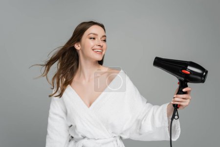 happy young woman with shiny hair using hair dryer isolated on grey 