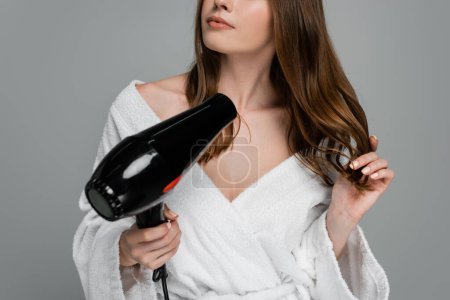 cropped view of young woman with shiny hair using hair dryer isolated on grey 